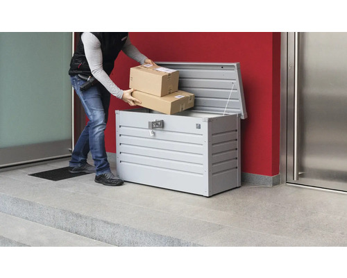 Paketzusteller legt Pakete in eine Paketbox aus Metall