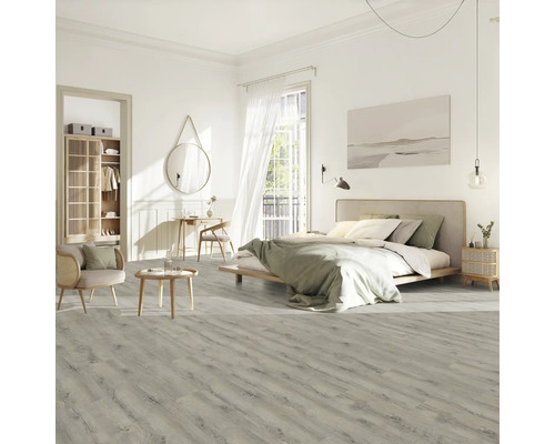 Heller Schlafzimmerraum mit Bett, Stuhl, Tisch und Laminatboden in Holzoptik.