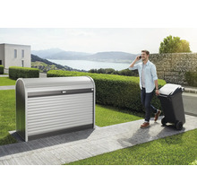 Mülltonnenbox aus Metall mit Rolltor im Garten, Mann telefoniert und zieht Mülltonne