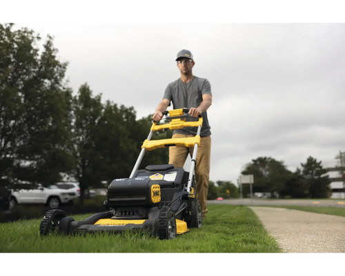 Mann schiebt einen gelben und schwarzen Rasenmäher im Garten.
