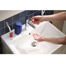 Waschbecken mit Armatur und laufendem Wasser, im Hintergrund Badaccessoires