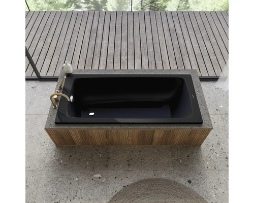 Schwarze Badewanne eingebaut in eine Ablage mit Armatur und Badeprodukt, umgeben von Holzboden