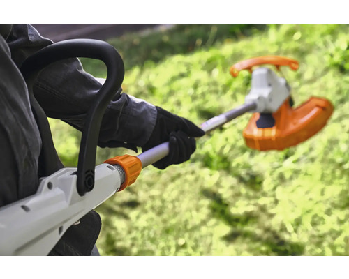 Person bedient einen Rasentrimmer im Garten.