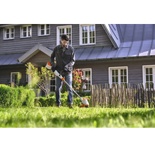 Mann arbeitet mit einem Akku-Rasentrimmer im Garten vor einem Haus.