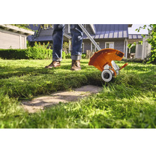 Eine Person trimmt Rasen mit einem Rasentrimmer im Garten.