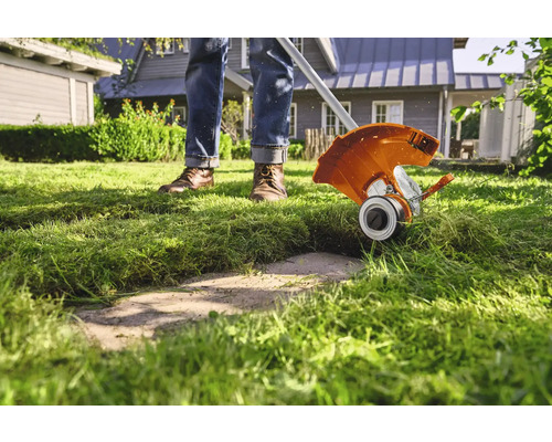 Eine Person trimmt Rasen mit einem Rasentrimmer im Garten.