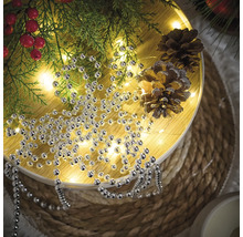 Dekoration mit Silberperlenkette, Tannenzweigen und Tannenzapfen auf einem runden Tisch.