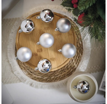 Dekorative silberfarbene Weihnachtskugeln auf einem Holzteller