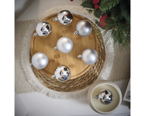 Dekorative silberfarbene Weihnachtskugeln auf einem Holzteller