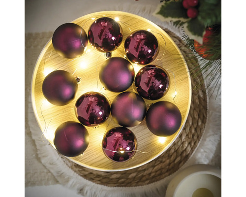 Dekorative violette Weihnachtskugeln mit Lichterkette auf einem Tablett