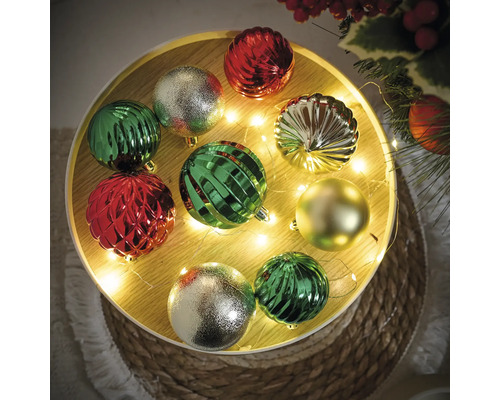 Dekorative Weihnachtskugeln in Grün, Silber und Rot auf einem dekorierten Tisch.