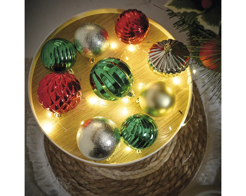 Dekorative Weihnachtskugeln in Grün, Rot und Gold auf einem runden Tablett mit Lichterkette.