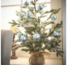 Dekorativer kleiner Weihnachtsbaum mit Christbaumkugeln im Jutesack auf Fensterbank