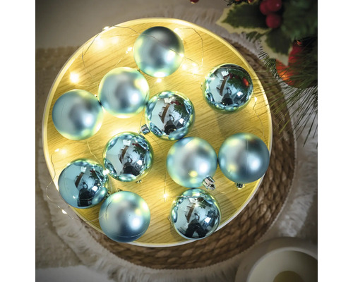 Dekorative, blaue Weihnachtskugeln mit Lichterkette auf einem Teller