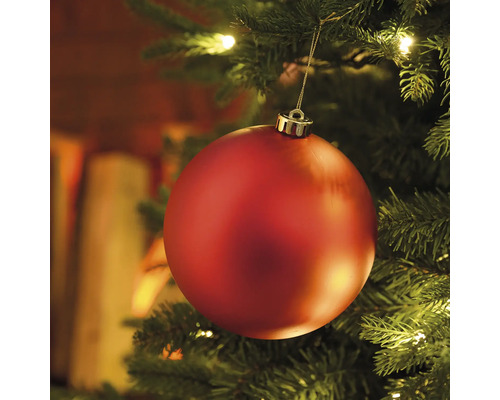 Nahaufnahme einer roten Weihnachtskugel an einem Weihnachtsbaum mit Lichtern
