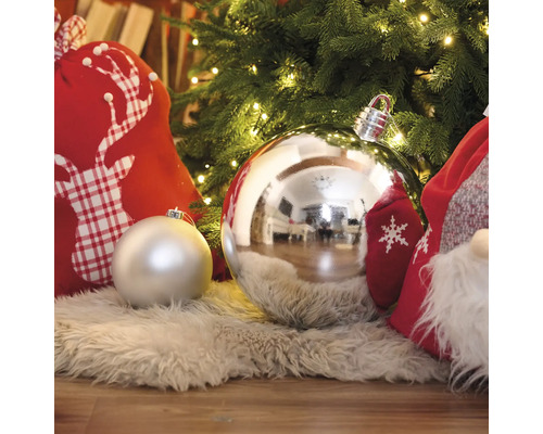 Dekorative Weihnachtskugeln unter einem beleuchteten Weihnachtsbaum mit Geschenksäcken auf einem Teppich