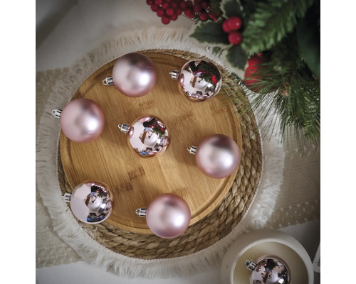 Anordnung von rosa Weihnachtskugeln auf einem Holzteller mit Tannenzweigen und Dekoration
