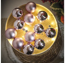 Dekorative Weihnachtskugeln in Rosa auf einem Holztablett mit Lichtern
