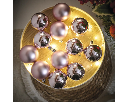 Dekorative Weihnachtskugeln in Rosa auf einem Holztablett mit Lichtern