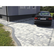 Einfahrt mit grauem Pflasterstein und Entwässerungsrinne vor einem Haus mit geparktem Auto