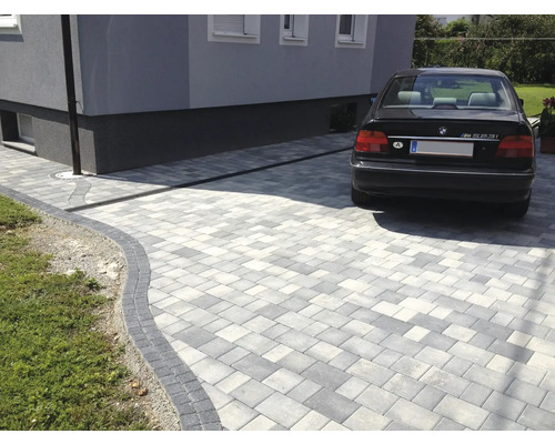 Gepflasterte Einfahrt mit Entwässerungsrinne und einem geparkten Auto.