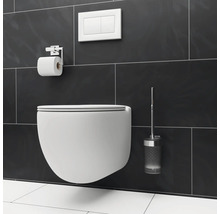 Wandhängendes WC mit Toilettenpapierhalter, Betätigungsplatte und WC-Bürste vor dunklem Fliesenhintergrund.