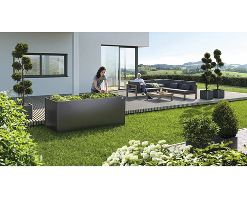 Gartenszene mit Hochbeet, bepflanzt von einer Frau, und einer Sitzecke mit Sofa und Tisch