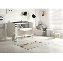 Helles Kinderzimmer mit Gitterbett, Stehlampe, Kinderstuhl und Teppich mit Tiermotiv