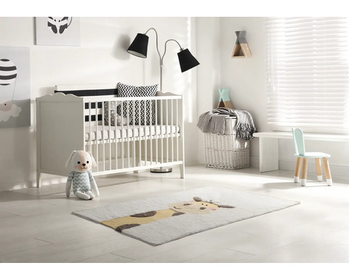 Helles Kinderzimmer mit Gitterbett, Stehlampe, Kinderstuhl und Teppich mit Tiermotiv