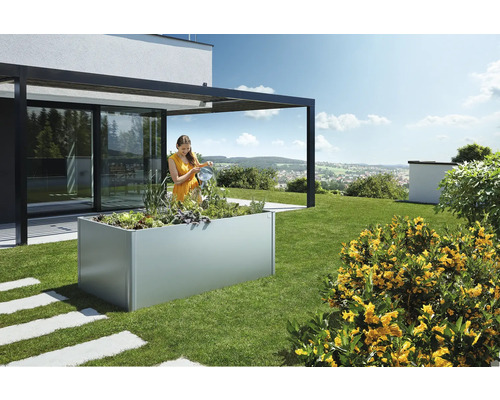 Frau gießt Pflanzen in einem Pflanzkasten im Garten