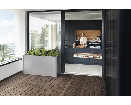 Szene mit einem Pflanzkasten auf einem Holzbalkon und einer Frau, die in einer Küche steht