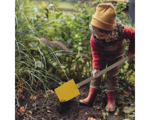 Kind mit gelbem Spaten gräbt im Garten