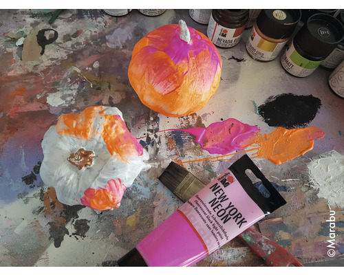Bemalte Kürbisse mit Farbe, Pinsel und Farbtuben auf einer Arbeitsfläche.