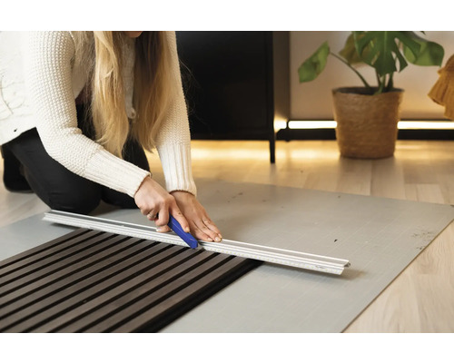 Frau schneidet Akustikpaneel mit Schneidwerkzeug auf Schneideunterlage