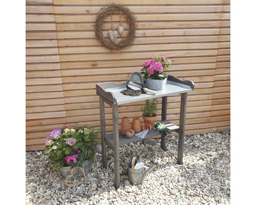 Gartenszene mit Anzuchttisch, Pflanzen und Gartengeräten auf Kies