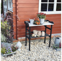 Gartenszene mit einem Gartentisch vor einem Gartenhaus, dekoriert mit Blumen und Gartenzubehör.