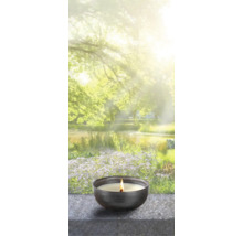 Brennende Duftkerze in einer Schale vor einem verschwommenen Gartenteich