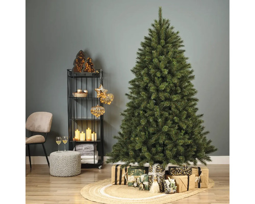 Dekorierter Weihnachtsbaum mit Geschenken auf einem geflochtenen Teppich in einem Wohnzimmer.