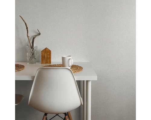 Szene mit einem Tisch, Stuhl, Tasse, Vase und Dekoration vor einer Wandtapete.