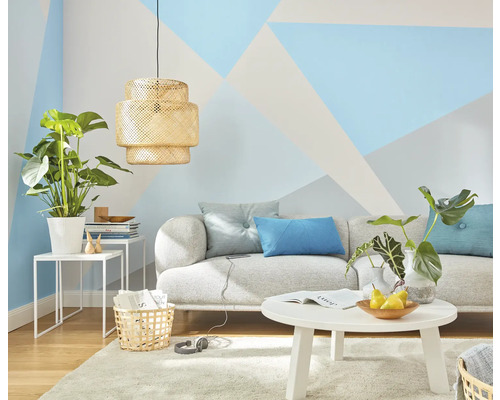 Wohnzimmer mit Sofa, Tisch, Lampe und Zimmerpflanzen vor einer Wand mit geometrischen Mustern