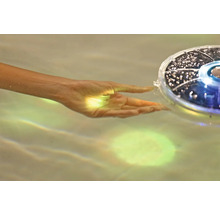 Hand berührt eine schwimmende Solarleuchte im Wasser.