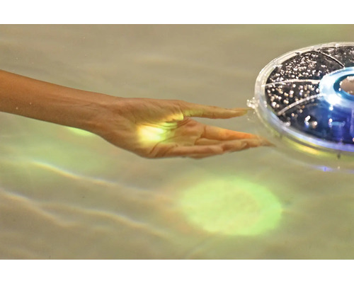 Hand berührt eine schwimmende Solarleuchte im Wasser.