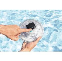 Eine Hand bedient einen runden Poolscheinwerfer mit Pumpe vor einem Pool.