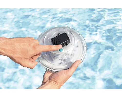 Eine Hand bedient einen runden Poolscheinwerfer mit Pumpe vor einem Pool.