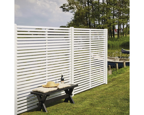 Weiße Zaunelemente mit horizontalen Lamellen neben einer Sitzbank im Garten