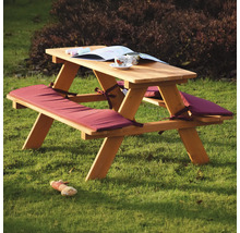 Picknicktisch aus Holz mit Sitzkissen, Buch und Spielzeug auf dem Rasen