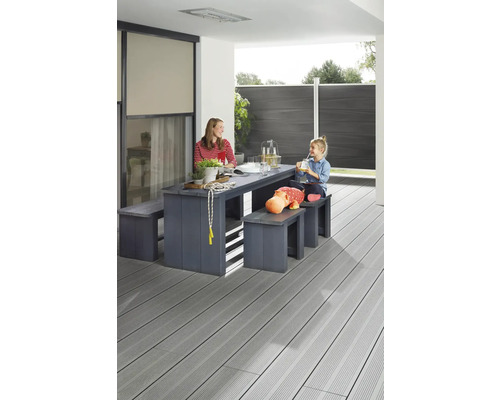 Familie sitzt an einem Holztisch mit Bänken auf einer Terrasse mit Holzboden