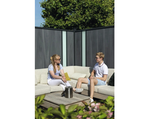 Ein junges Paar sitzt auf einer Loungegarnitur vor einem Sichtschutzzaun mit Glaselementen.
