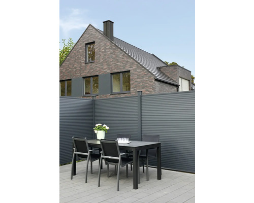 Gartenszene mit Tisch, Stühlen und Zaun vor einem Wohnhaus.