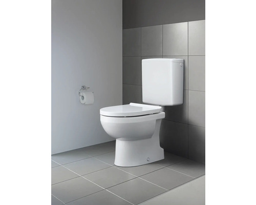 Weiße Toilette mit Aufputzspülkasten vor grauer Wandfliese und Toilettenpapierhalter